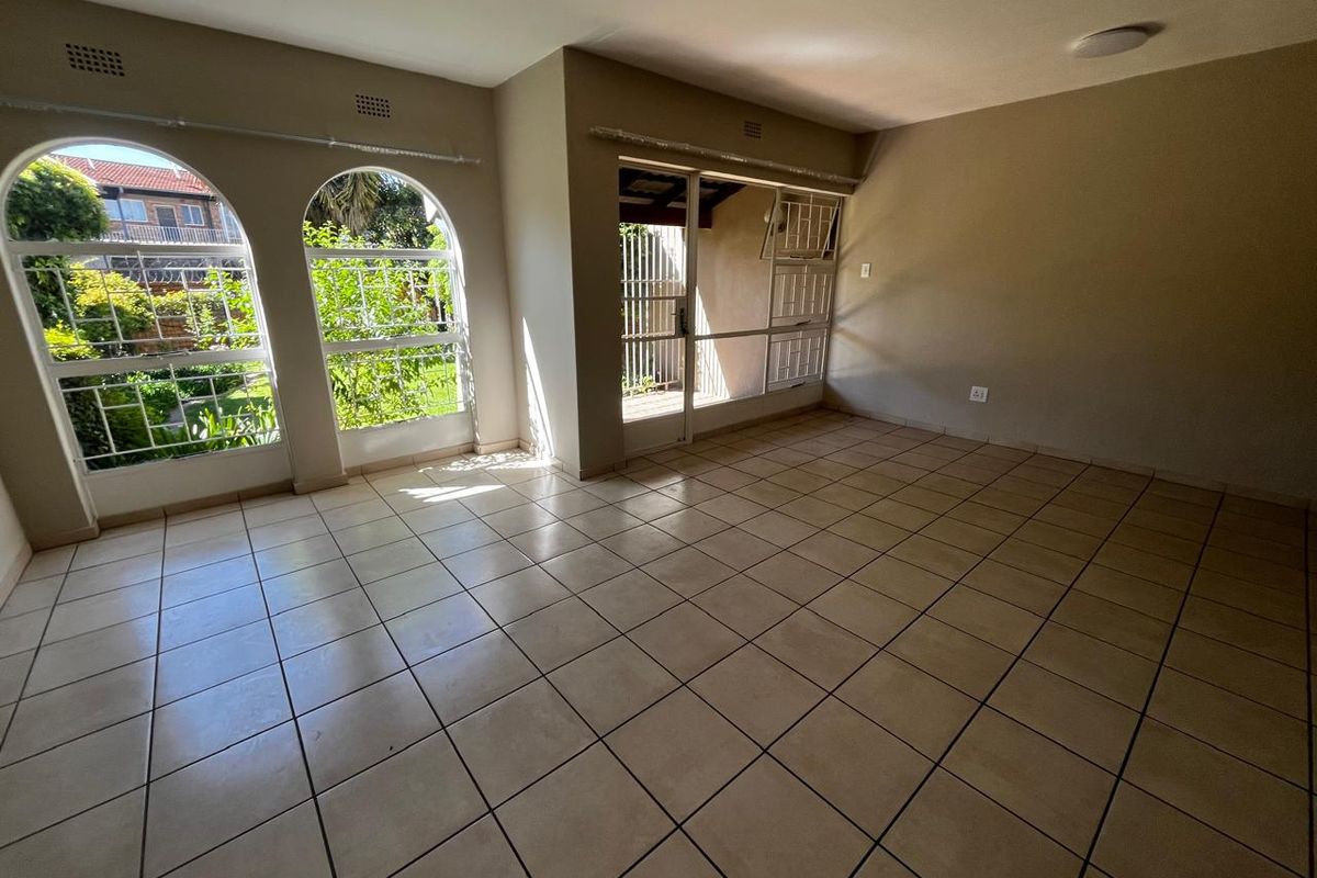 Spacious, empty living area featuring neutral tiled flooring, distinctive arched windows, and direct access to an outdoor patio through a sliding glass door.