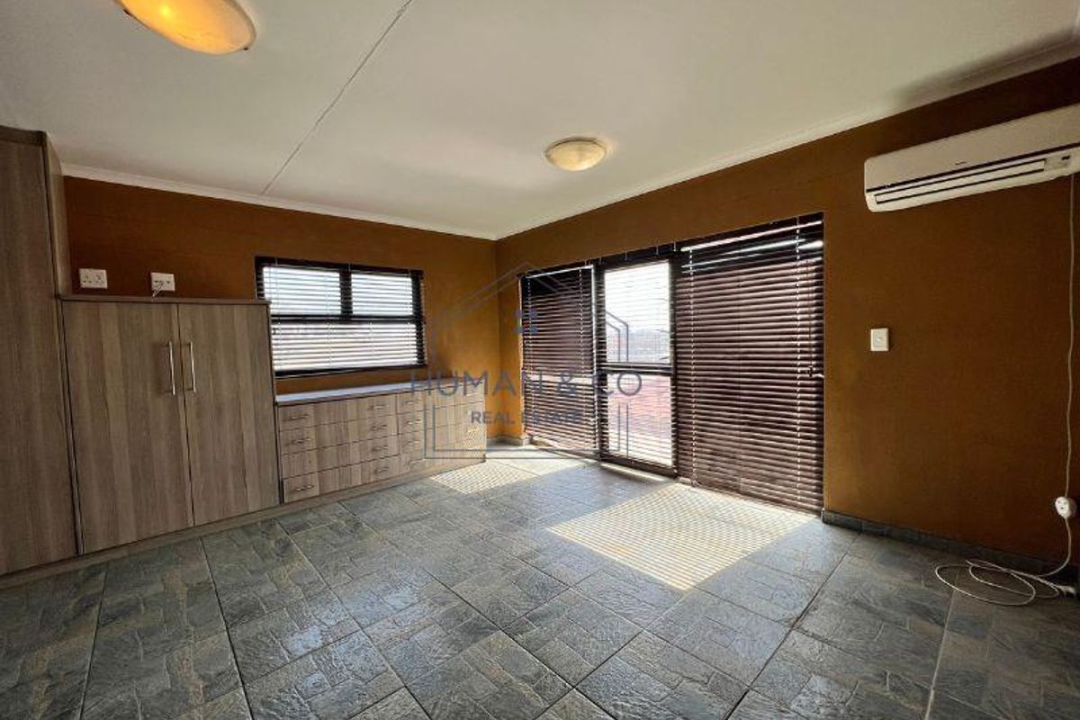 A spacious room featuring built-in cabinetry, tiled flooring, large windows with blinds, and a wall-mounted air conditioning unit.