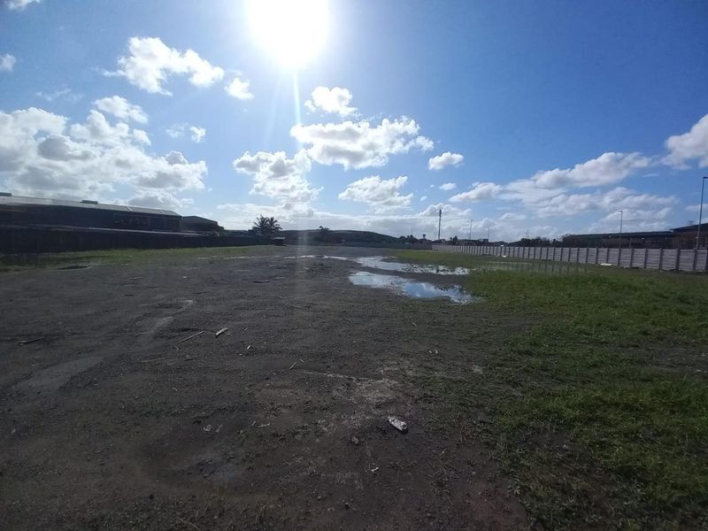 A large, undeveloped industrial plot featuring an unpaved surface and perimeter concrete boundary walling under a clear sky.