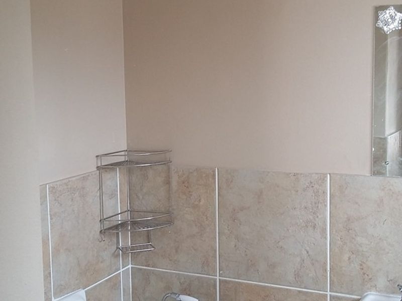 A functional bathroom featuring a bathtub with shower mixer, wall tiling, and a wall-mounted washbasin.