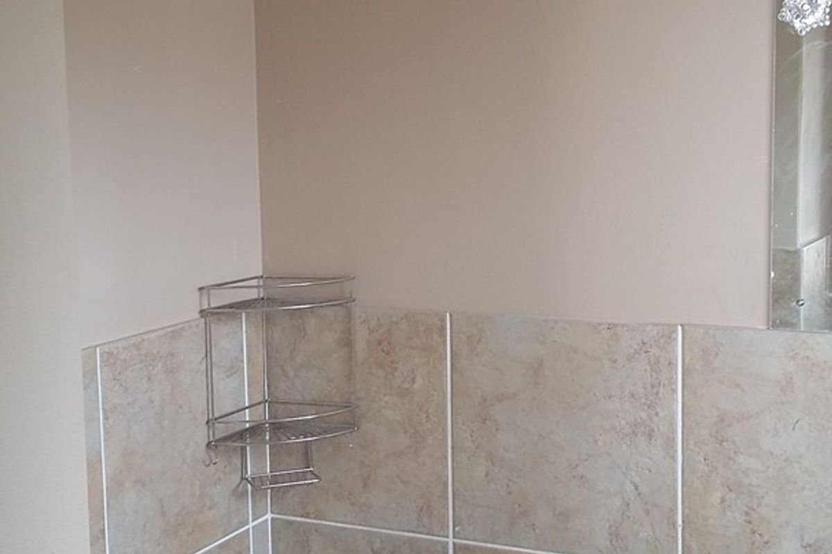 A functional bathroom featuring a bathtub with shower mixer, wall tiling, and a wall-mounted washbasin.