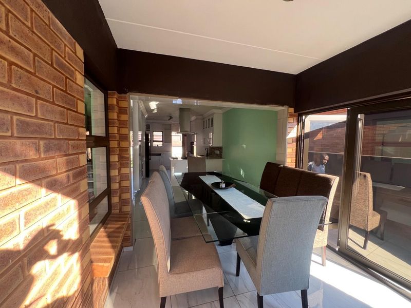 Open plan dining area featuring exposed brick walls and large sliding glass doors, leading into a modern kitchen space with tiled flooring.