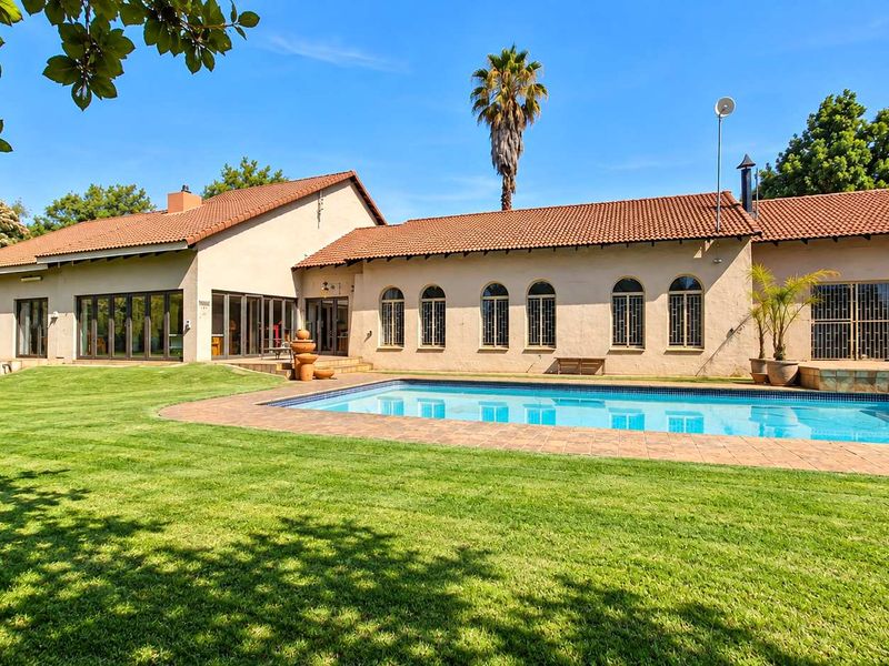 Spacious rear garden featuring a swimming pool with tiled surround, set against a well-maintained single-story residence with arched windows and terracotta roof tiles.