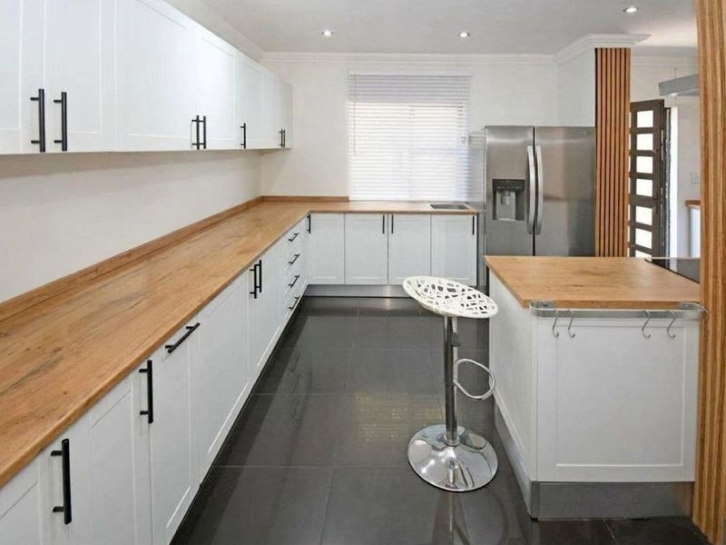 Modern kitchen featuring white shaker-style cabinetry, warm wooden countertops, dark tiled flooring, and integrated appliances in a clean, well-maintained space.