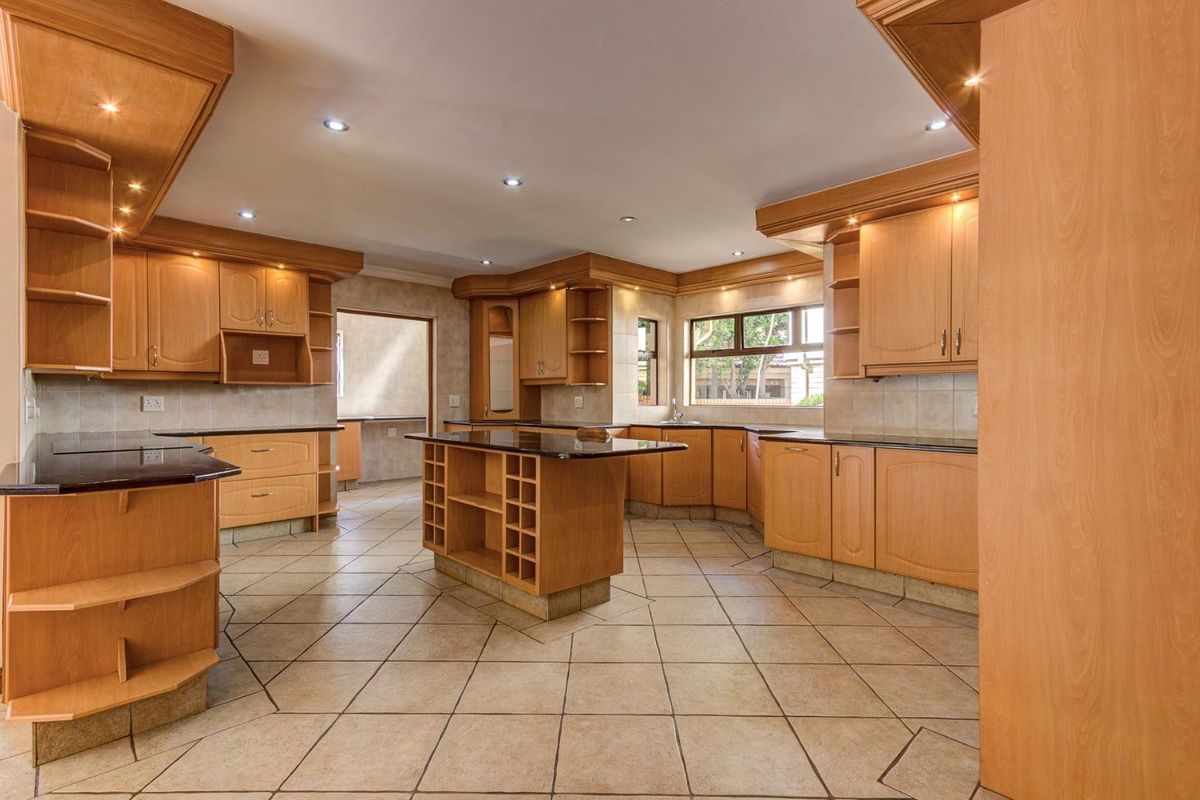 Spacious kitchen featuring extensive wooden cabinetry, granite countertops, a central island, and tiled flooring, offering a functional layout with ample storage space.