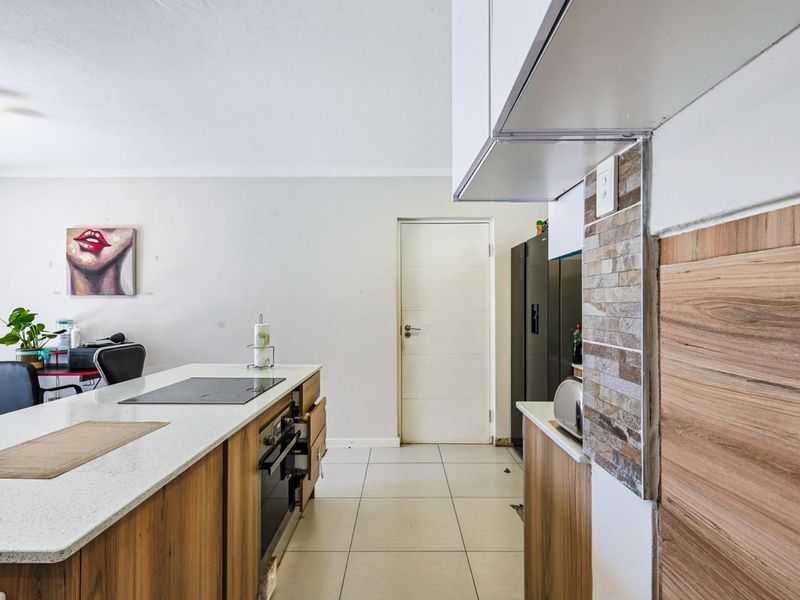 Modern kitchen featuring a central island with a built-in oven and hob, stone countertops, and tiled flooring, offering a functional open-plan layout.