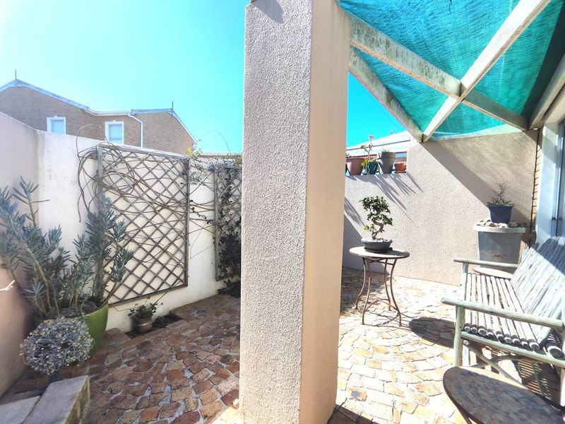A private outdoor patio area featuring paved flooring, a structural support pillar, and a shade cloth canopy, offering a cozy space for relaxation.