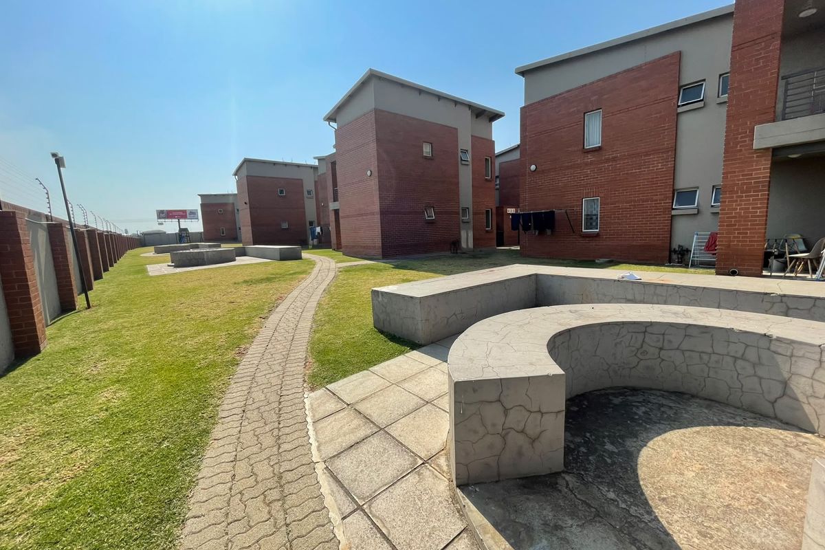 Communal outdoor area featuring a paved walkway, landscaped lawn, and built-in concrete seating between apartment blocks.