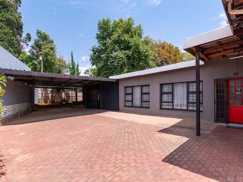 Front exterior view featuring a paved driveway, covered carport, and secure entrance with aluminium window frames.