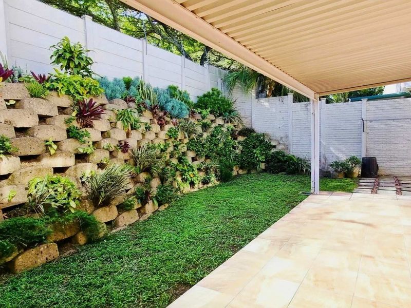 A covered patio area featuring tiled flooring and a landscaped retaining wall, providing a pleasant outdoor space for relaxation.