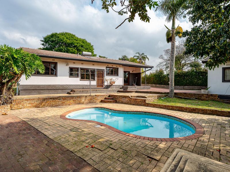 Rear exterior view featuring a swimming pool, brick paved patio area, and a single-story house with a solar water heater.