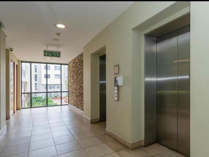 A modern apartment building hallway featuring stainless steel elevator doors, tiled flooring, and a decorative stone feature wall with large windows.