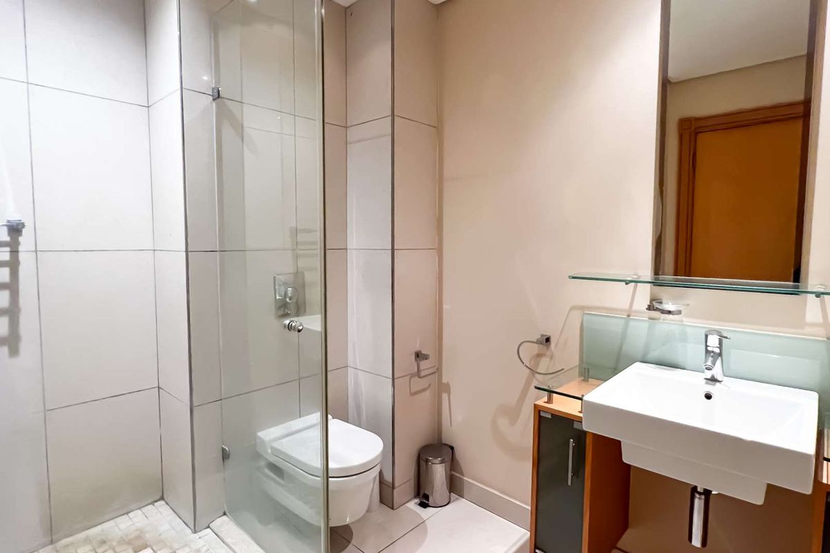Modern bathroom featuring a glass-enclosed shower, wall-mounted toilet, and a vanity unit with a basin and integrated mirror.