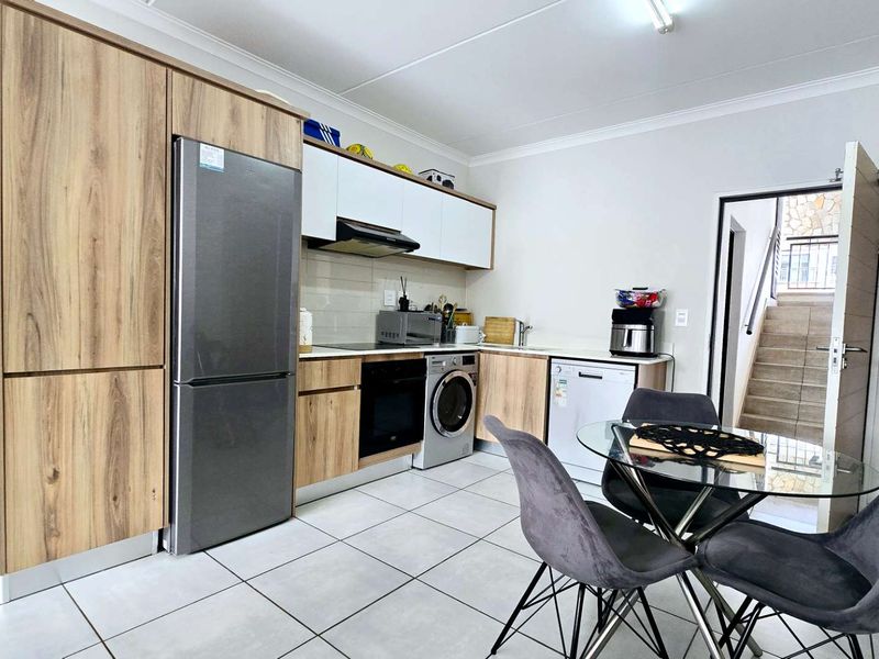 Modern kitchen featuring light wood-grain cabinetry, integrated appliances, tiled flooring, and a clean, functional layout with direct access to the stairwell.