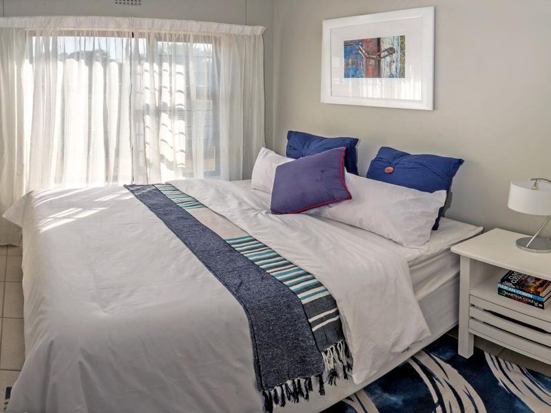 A well-maintained bedroom featuring neutral wall tones, tiled flooring, and large windows with sheer curtains allowing for natural light.