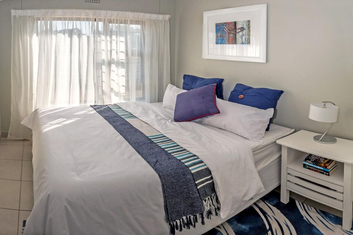 A well-maintained bedroom featuring neutral wall tones, tiled flooring, and large windows with sheer curtains allowing for natural light.