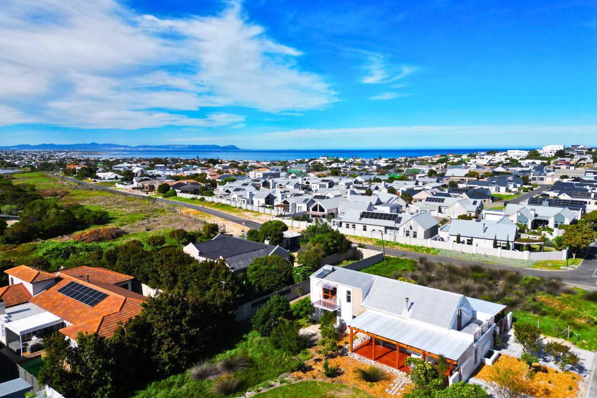 Aerial view of a residential property featuring a metal roof, solar panels, and a covered patio, situated in a coastal neighborhood.