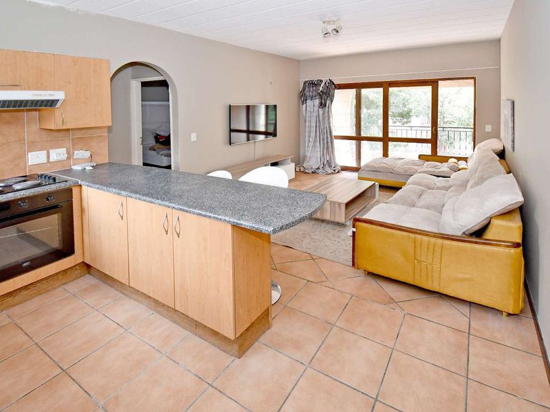 Open-plan living area featuring a kitchen with built-in cabinetry, granite countertops, and tiled flooring, leading to a sliding door with outdoor access.