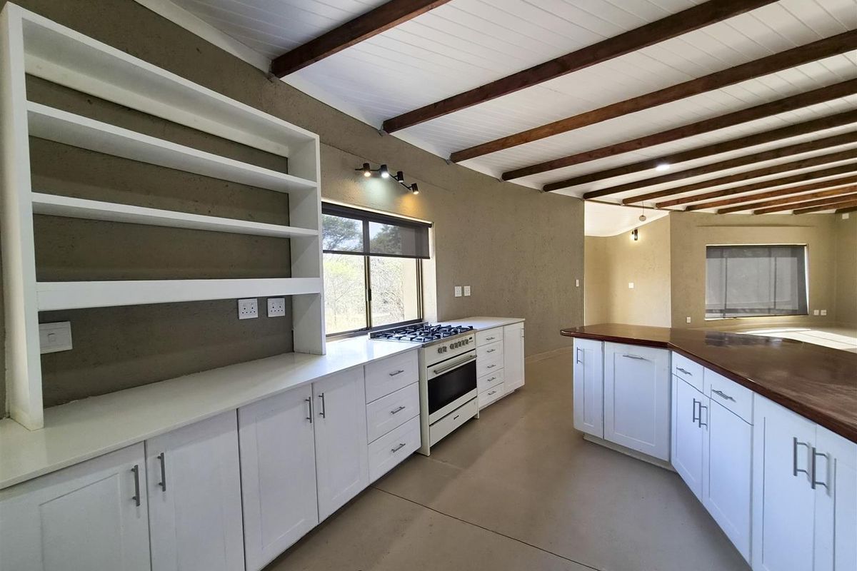 Spacious kitchen featuring white cabinetry, stone countertops, a gas stove, and exposed timber ceiling beams, offering a clean and functional layout.
