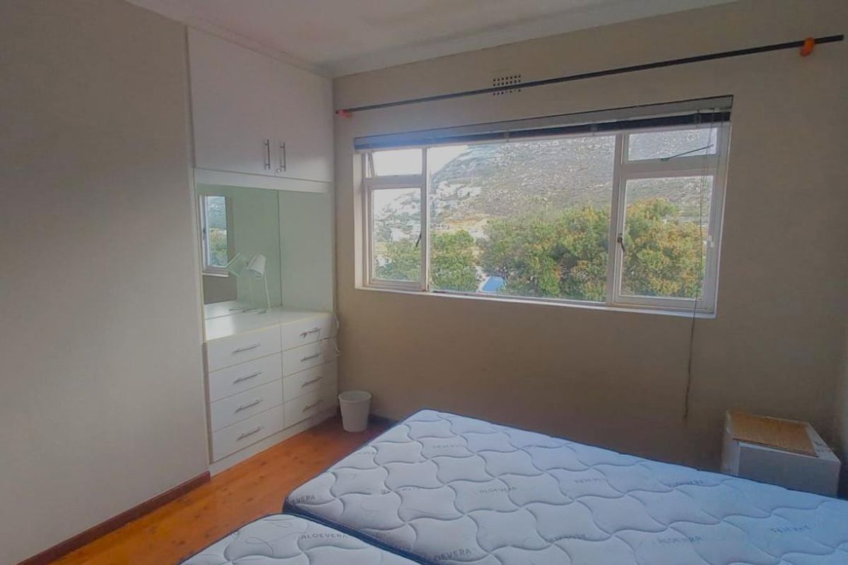 A bedroom featuring built-in cupboards with an integrated vanity mirror, wooden flooring, and large windows offering scenic views.