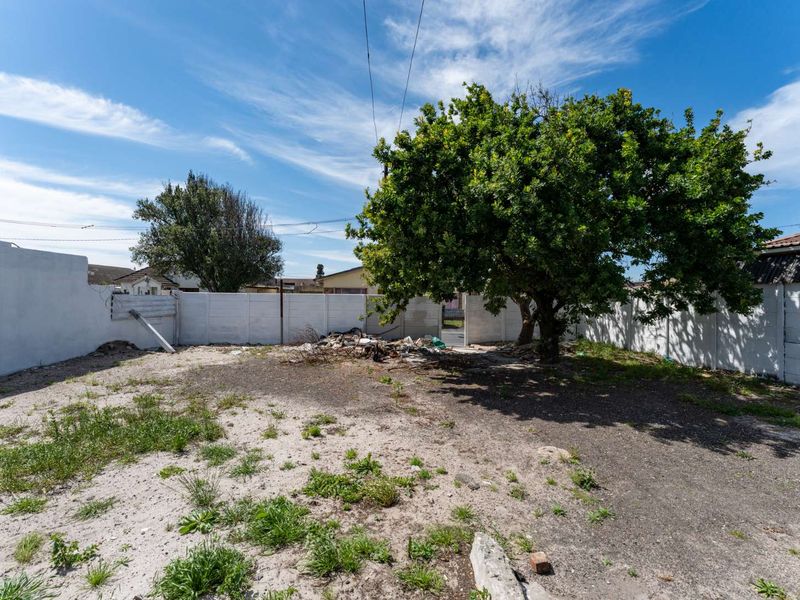A spacious rear yard area featuring a mature tree and perimeter precast concrete walling, currently requiring landscaping and debris removal.