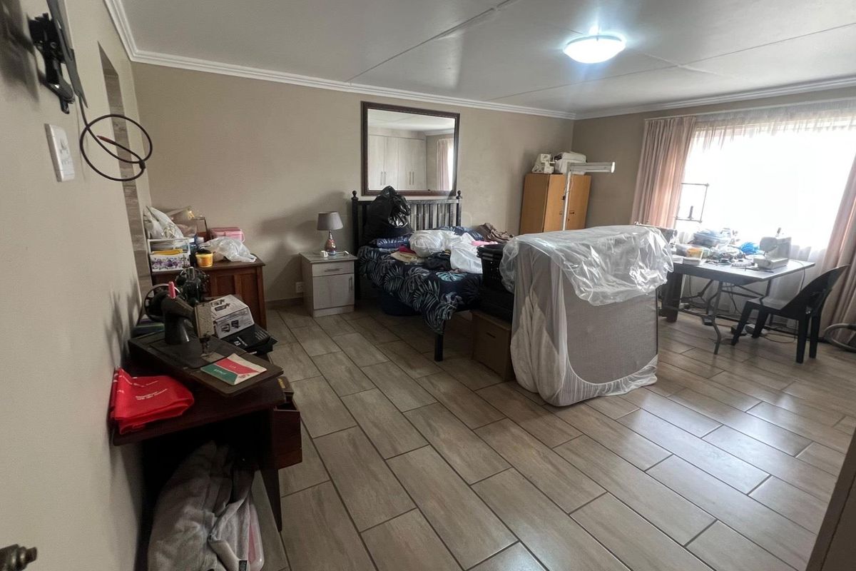 A spacious bedroom featuring tiled flooring, neutral wall tones, and a large window allowing natural light, providing a versatile layout for sleeping and storage.
