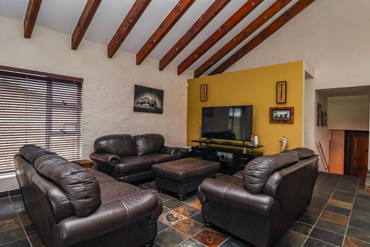 Spacious living room featuring high vaulted ceilings with exposed timber beams, slate tile flooring, and a prominent feature wall.