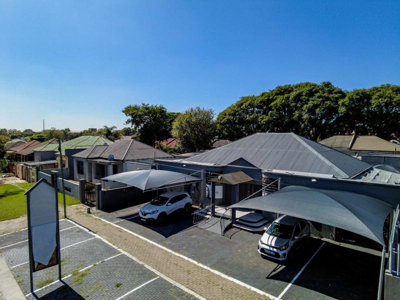 Aerial view of an office property featuring paved parking areas, shade cloth carports, and a well-maintained building exterior with a metal roof.