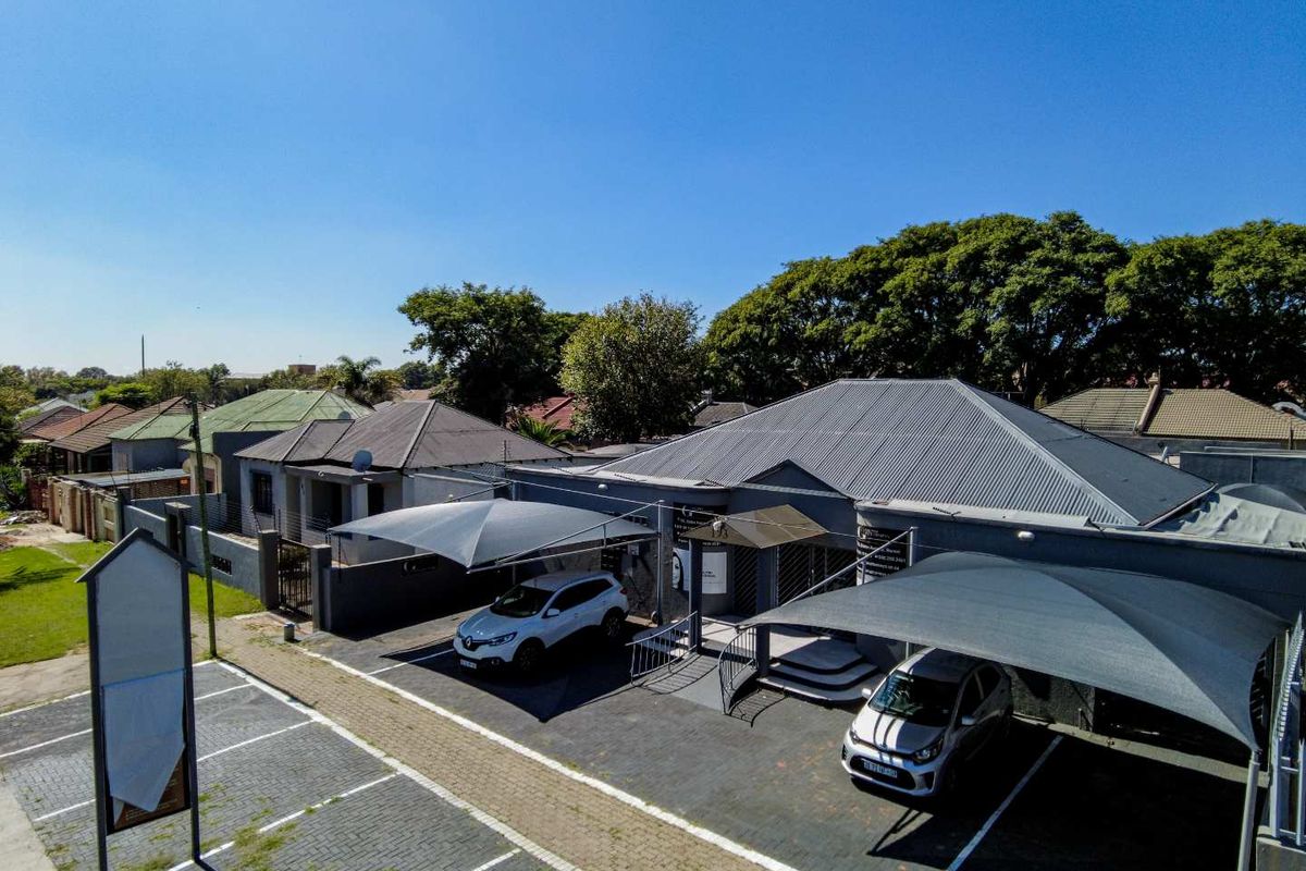 Aerial view of an office property featuring paved parking areas, shade cloth carports, and a well-maintained building exterior with a metal roof.