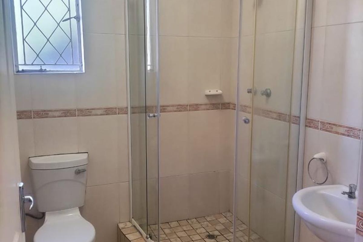 A functional bathroom featuring a curved glass shower enclosure, pedestal sink, and ceramic toilet with neutral wall and floor tiling.