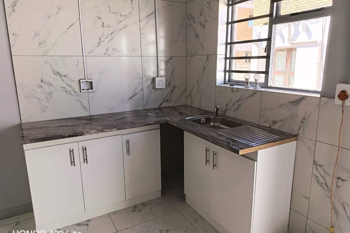 A compact kitchen area featuring marble-effect wall tiling, white base cabinetry, a stainless steel sink, and surface-mounted electrical wiring.