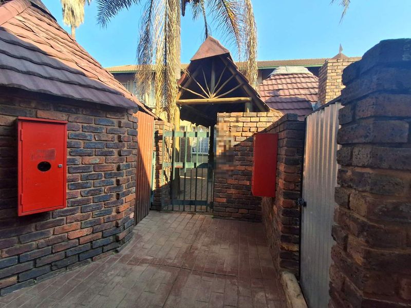 A gated entrance area featuring face brick walls, paved flooring, and a timber-framed roof structure leading to the townhouse entrance.