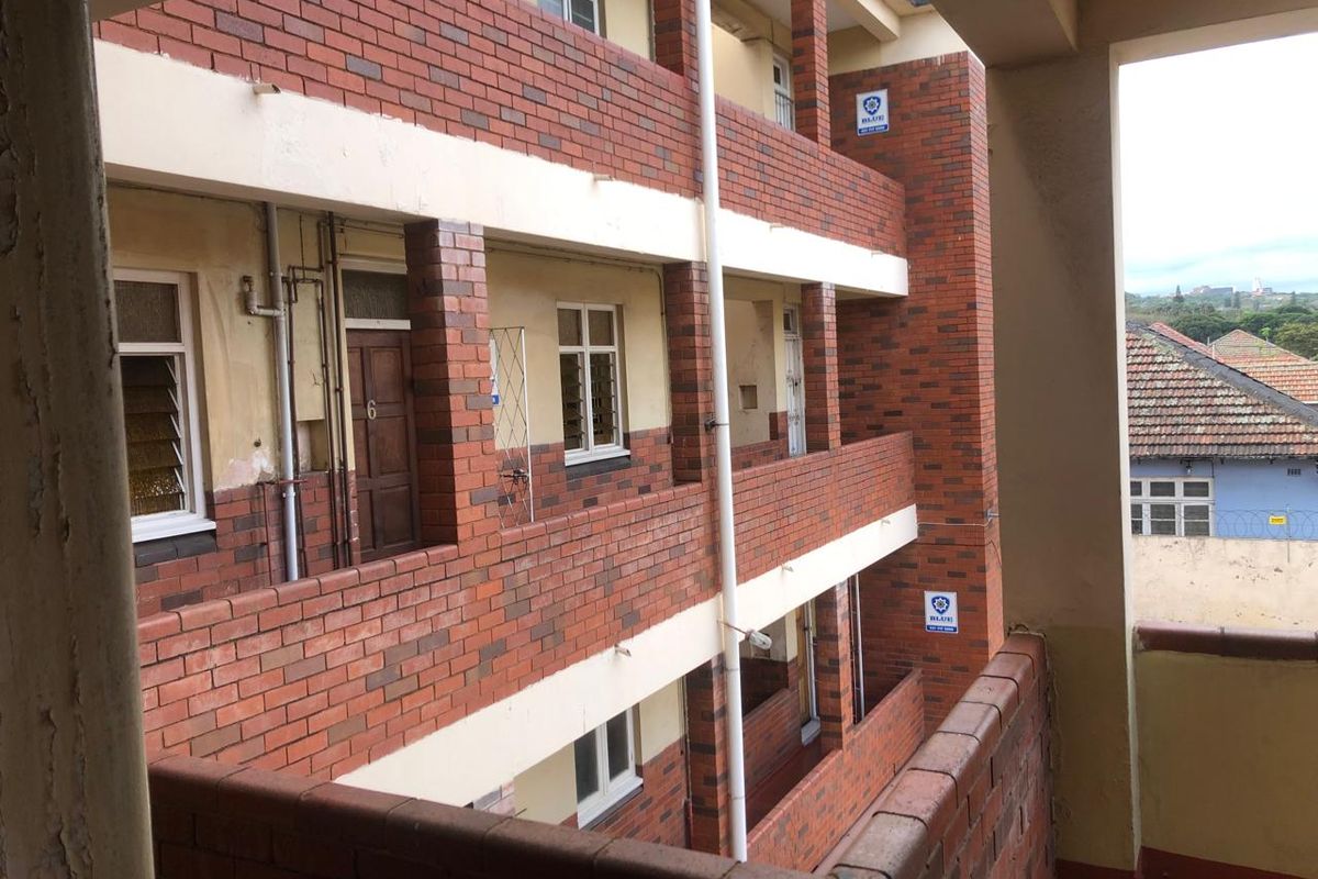 Exterior view of a multi-story apartment building featuring face brick facade, external walkways, and security signage.
