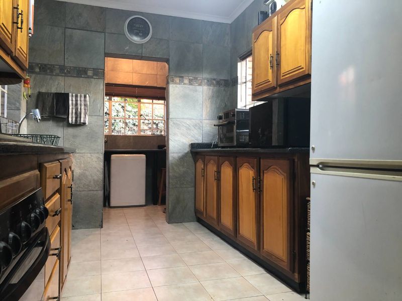 A functional kitchen featuring wooden cabinetry, granite countertops, and stone tile wall finishes, with an adjacent scullery area visible through the doorway.