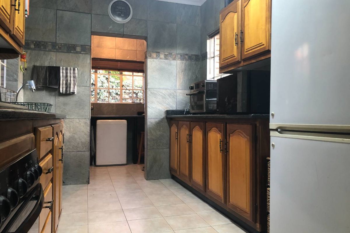 A functional kitchen featuring wooden cabinetry, granite countertops, and stone tile wall finishes, with an adjacent scullery area visible through the doorway.