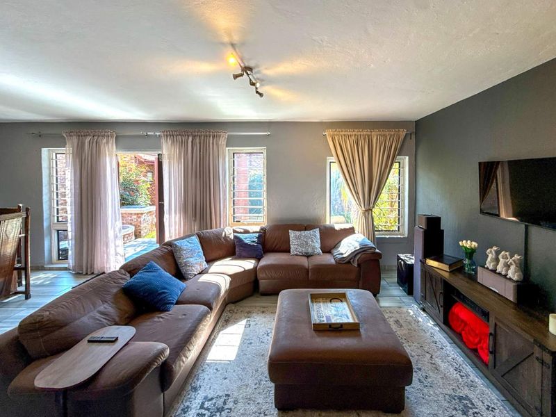 Spacious living room featuring tiled flooring, track lighting, and large windows with security bars, providing direct access to the outdoor patio area.