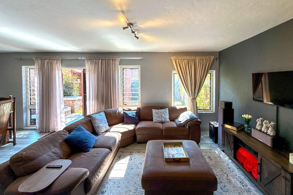 Spacious living room featuring tiled flooring, track lighting, and large windows with security bars, providing direct access to the outdoor patio area.