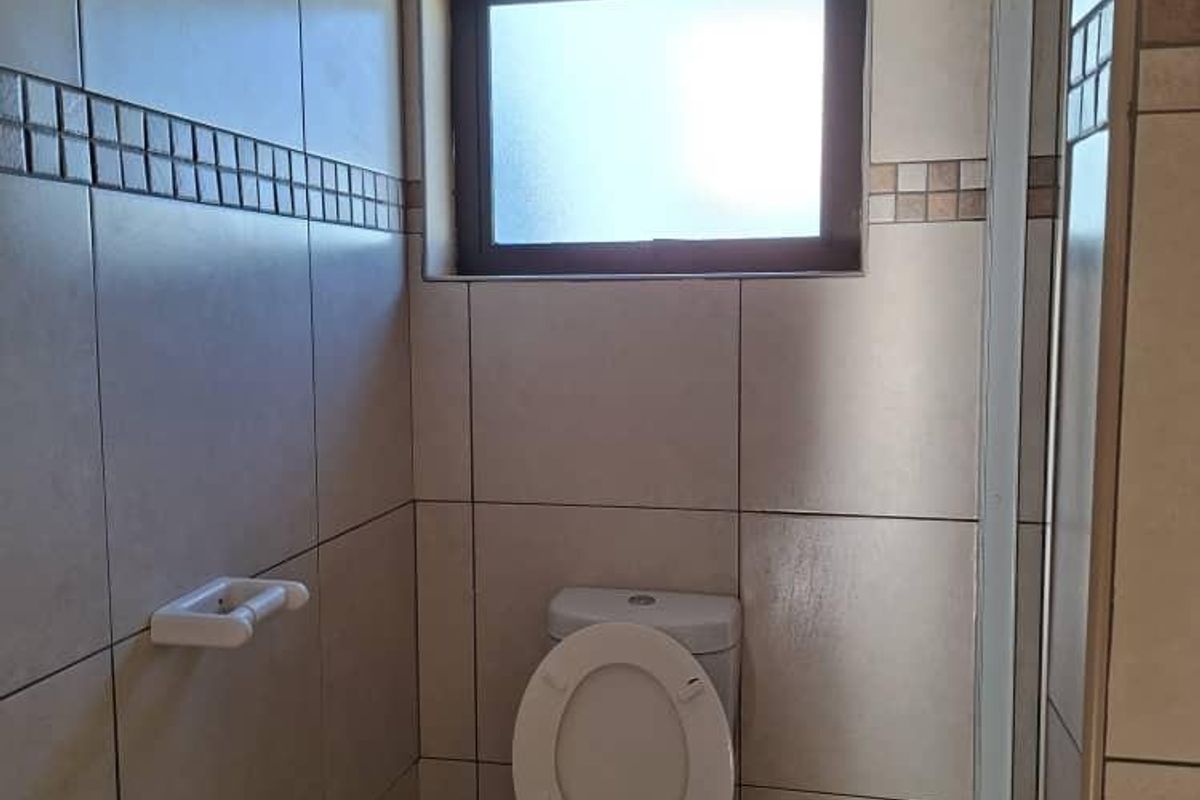 A functional bathroom featuring floor-to-ceiling wall tiles, a standard toilet, and a shower enclosure with a frosted glass window.