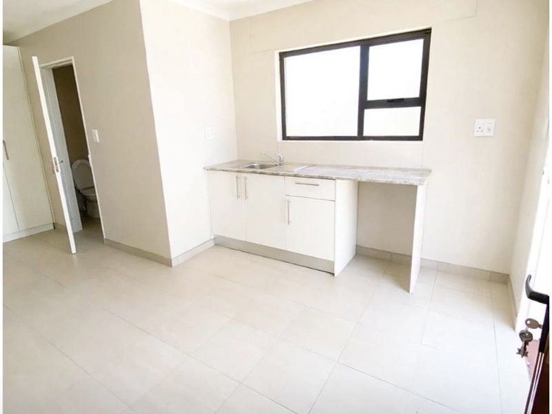 A clean, minimalist kitchen area featuring white built-in cabinetry, a stone countertop with an integrated sink, and neutral tiled flooring.