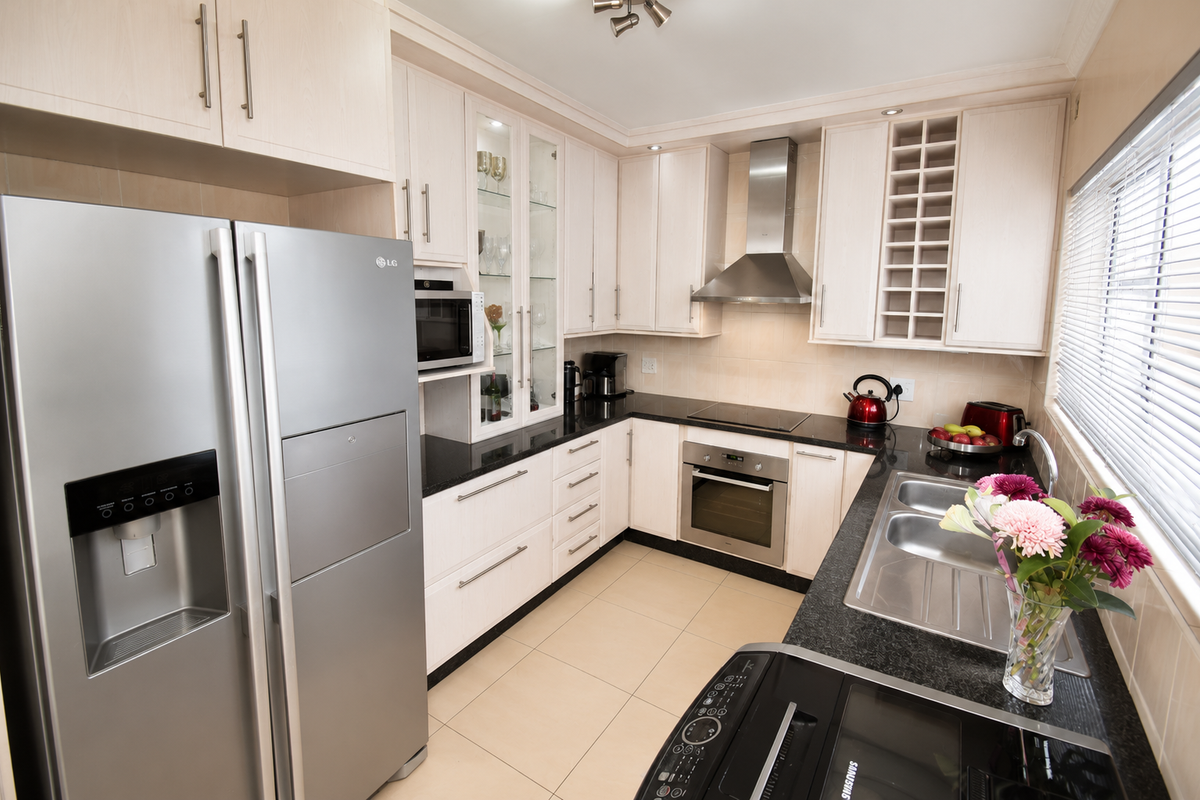 A well-maintained kitchen featuring light wood cabinetry, black granite countertops, stainless steel appliances, a built-in oven, and a glass-front display cabinet.