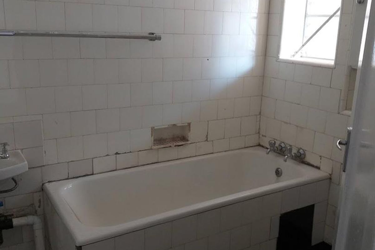 A dated bathroom featuring a built-in bathtub, wall-mounted basin, and tiled walls, requiring renovation to update the finishes and fixtures.