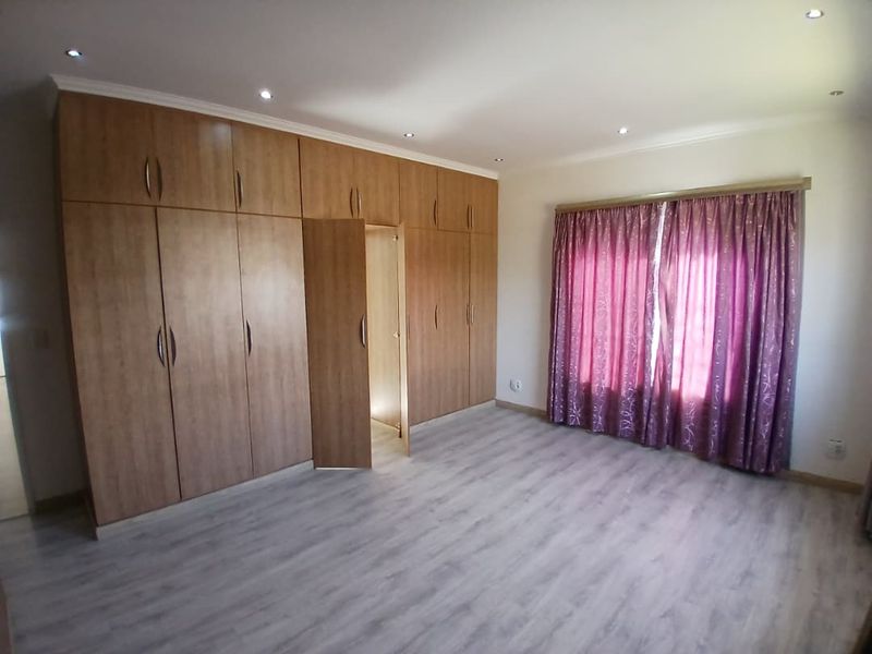Spacious bedroom featuring extensive built-in wooden cabinetry, modern light-toned laminate flooring, and recessed ceiling lighting.