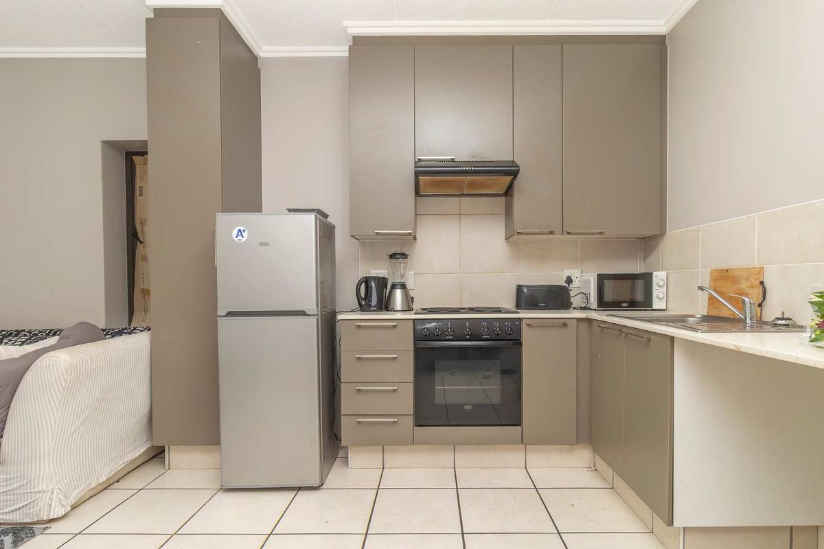 Compact kitchen featuring taupe cabinetry, built-in oven, extractor fan, and tiled flooring, providing a functional workspace within an open-plan layout.