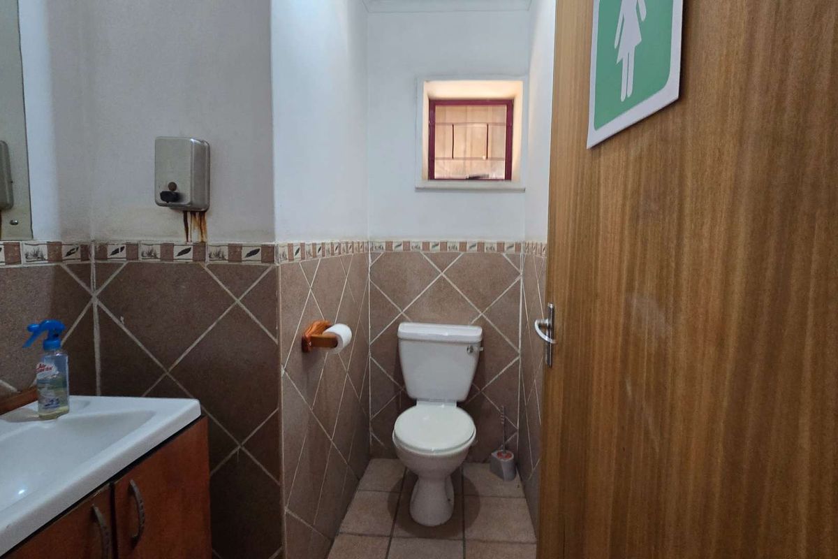 A functional industrial bathroom featuring a toilet, vanity basin, and tiled finishes, suitable for staff or visitor use.