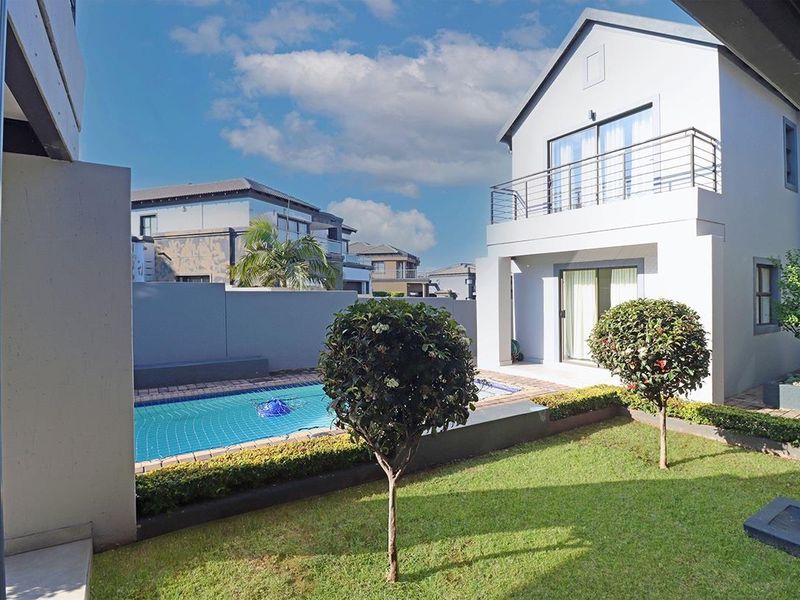 Rear view of the property featuring a private swimming pool, landscaped garden, and an upper-level balcony with modern architectural finishes.