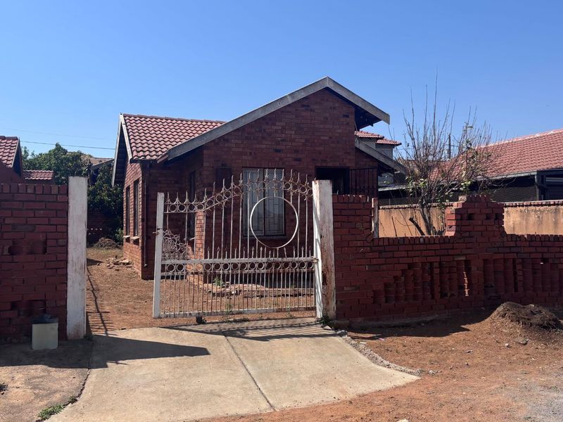 Front view of a face brick house featuring a tiled roof, wrought iron gate, and a brick boundary wall with an unpaved garden area.