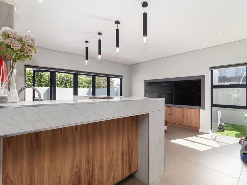 Modern open-plan living area featuring a marble-look kitchen island, sleek pendant lighting, built-in fireplace, and large stacker doors leading to the outdoor space.
