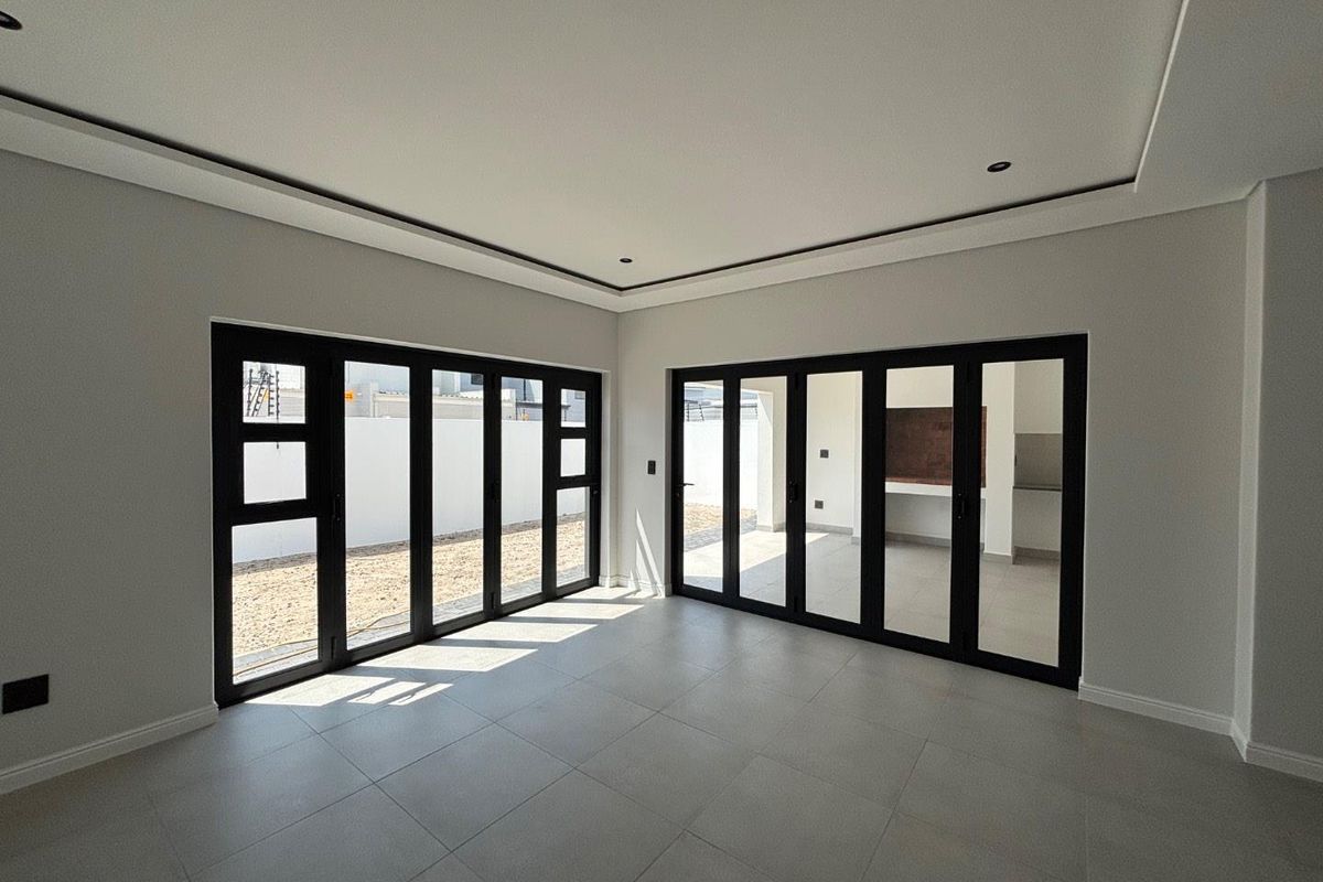 Spacious, modern living area featuring large black aluminium stacker doors that open onto an outdoor patio area, finished with neutral floor tiles.