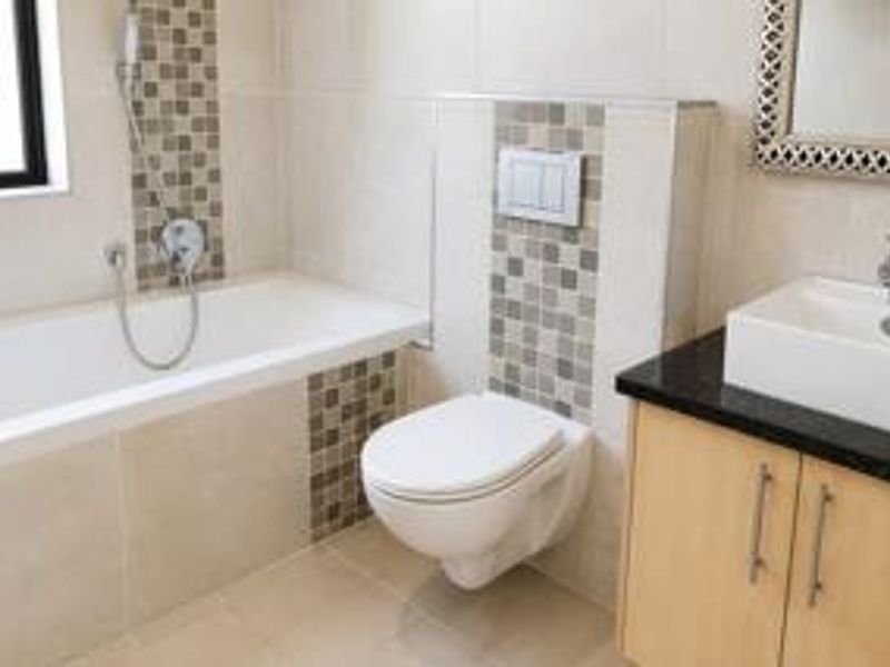 Modern bathroom featuring a wall-mounted toilet, built-in bathtub, and a vanity cabinet with a basin and mosaic tile detailing.