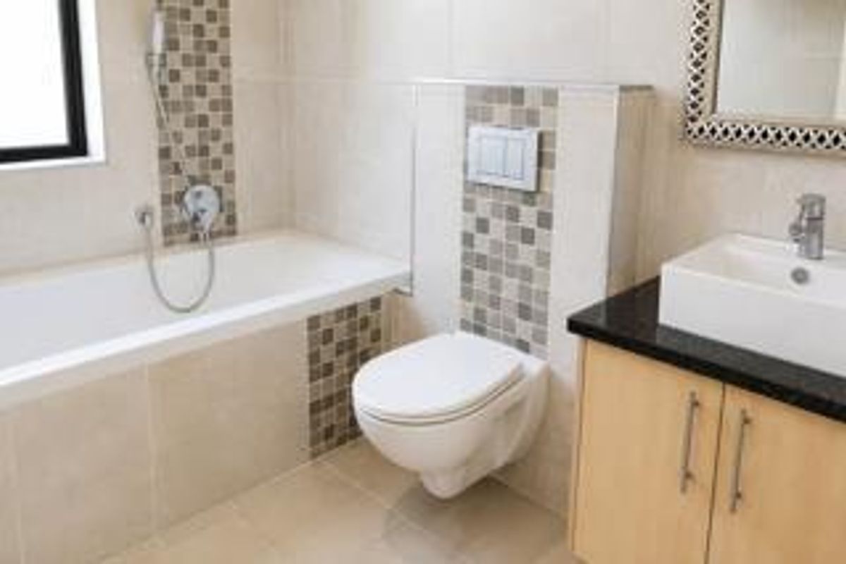 Modern bathroom featuring a wall-mounted toilet, built-in bathtub, and a vanity cabinet with a basin and mosaic tile detailing.